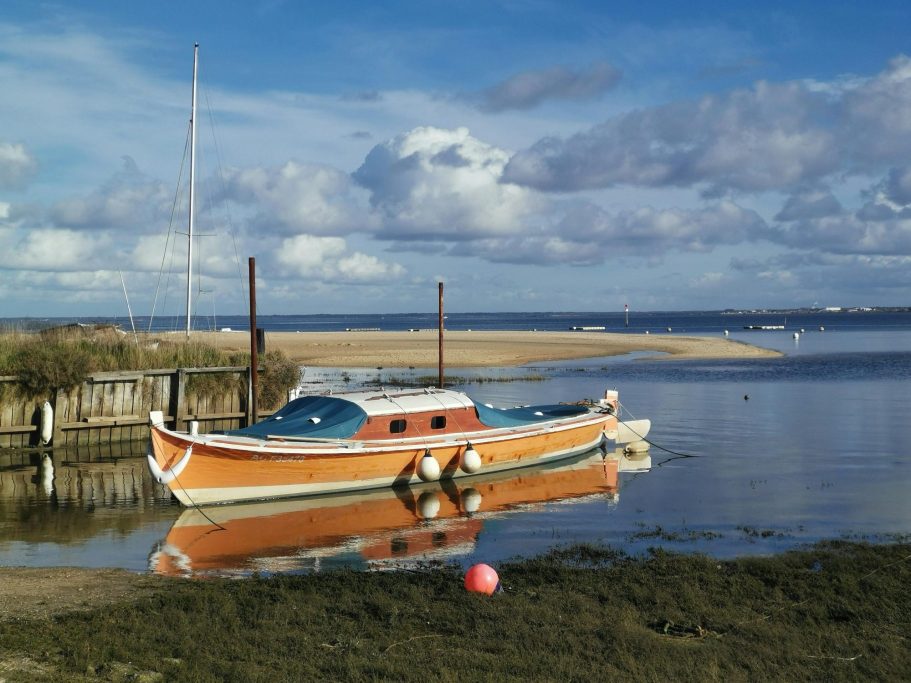 Bateau coloré amarré près d'une rive, avec ciel nuageux et eau calme.